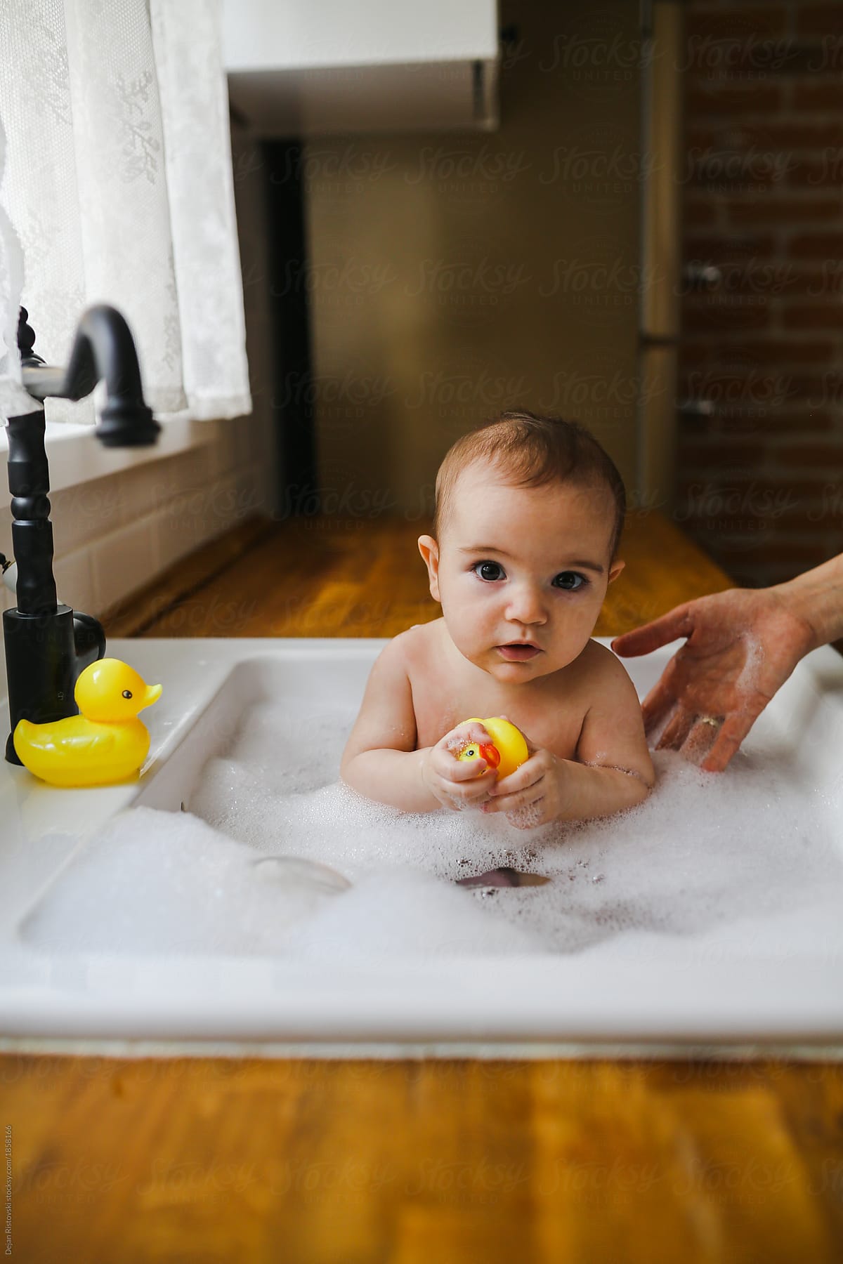 Baby having a bath in the kitchen sink by Dejan Ristovski